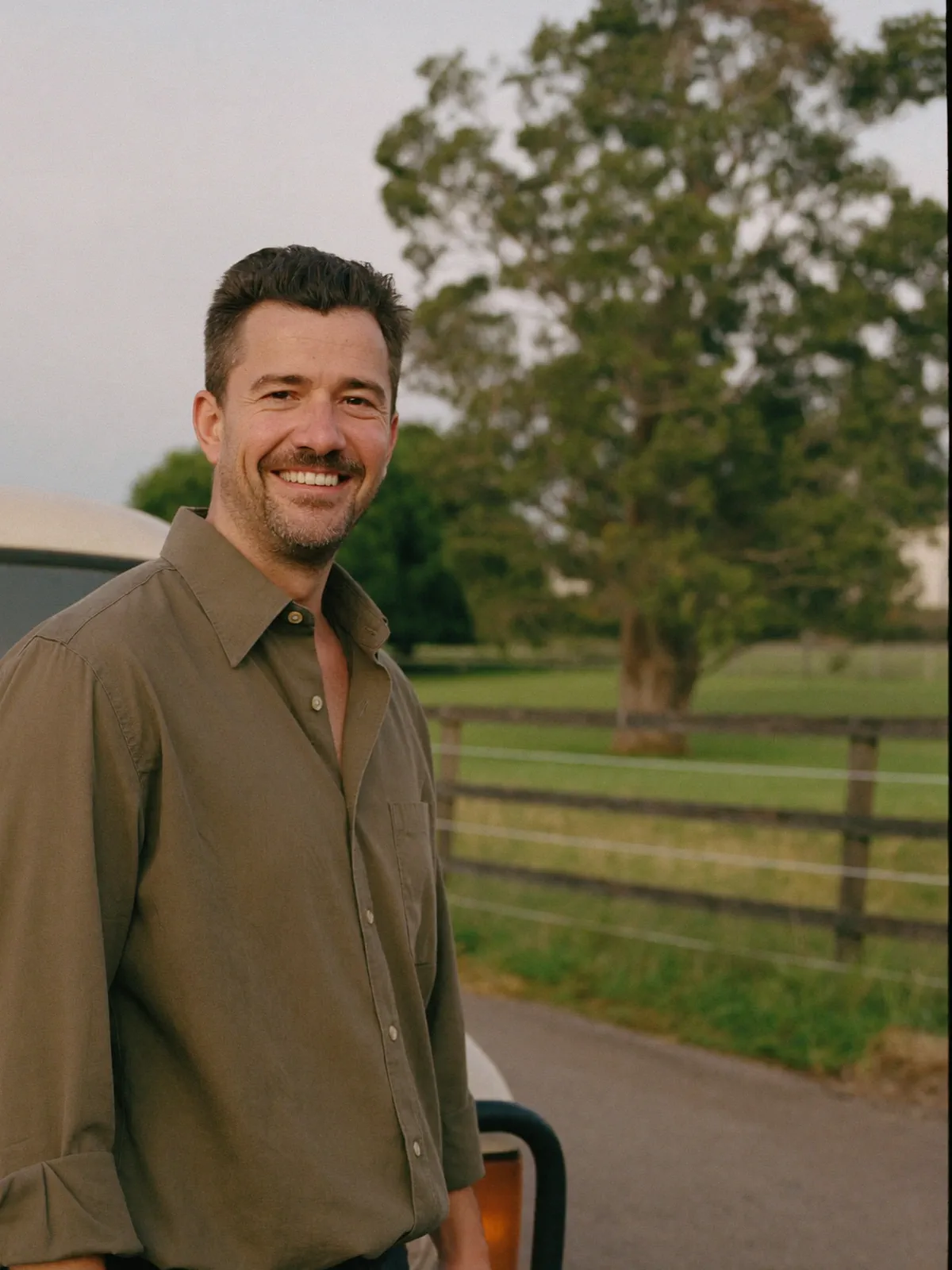 Ben, a mortgage broker in his late thirties in a rolled-sleeve olive shirt, standing outdoors at the edge of a country sports oval.